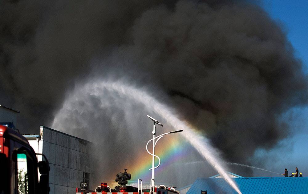 A rainbow appears on the water splayed from a fire engine as firemen extinguish a fire on a lumberyard at the south side of Beijing, China.
