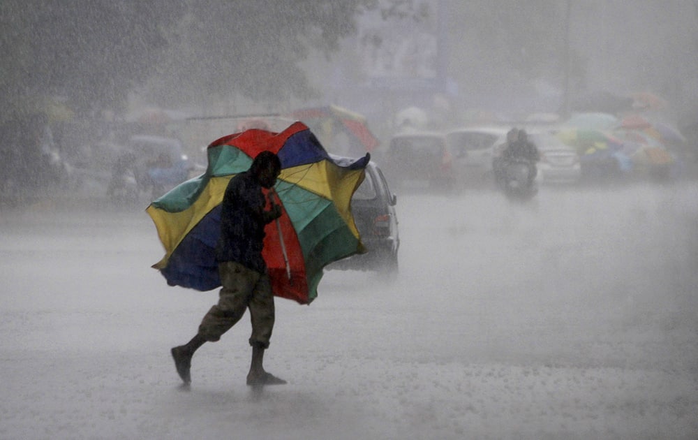 A gust of wind bends the umbrella of a street vendor crossing the road during a heavy downpour in Bhubaneswar.