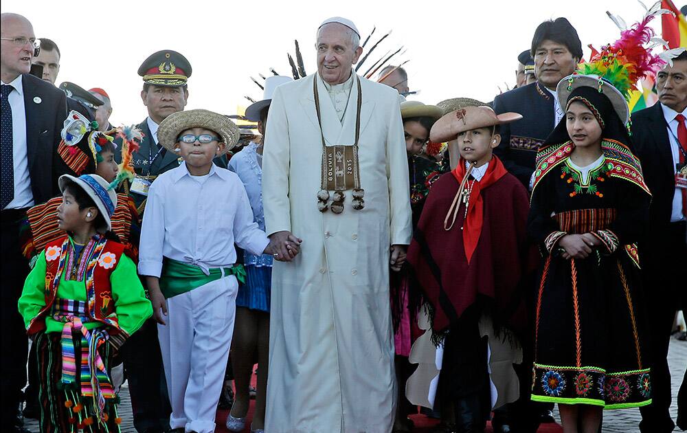 Pope Francis holds hands with children wearing traditional costumes as he walks with Bolivian President Evo Morales upon his arrival at the El Alto airport, Bolivia.