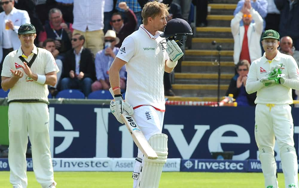 England's Joe Root kisses the badge in his helmet as he celebrates a century applauded by Australia's Brad Haddin and Shane Watson during day one of the first Ashes Test cricket match, in Cardiff, Wales.