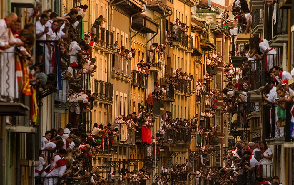 People watch as Jandilla fighting bulls and revelers run during the running of the bulls, at the San Fermin festival, in Pamplona, Spain.