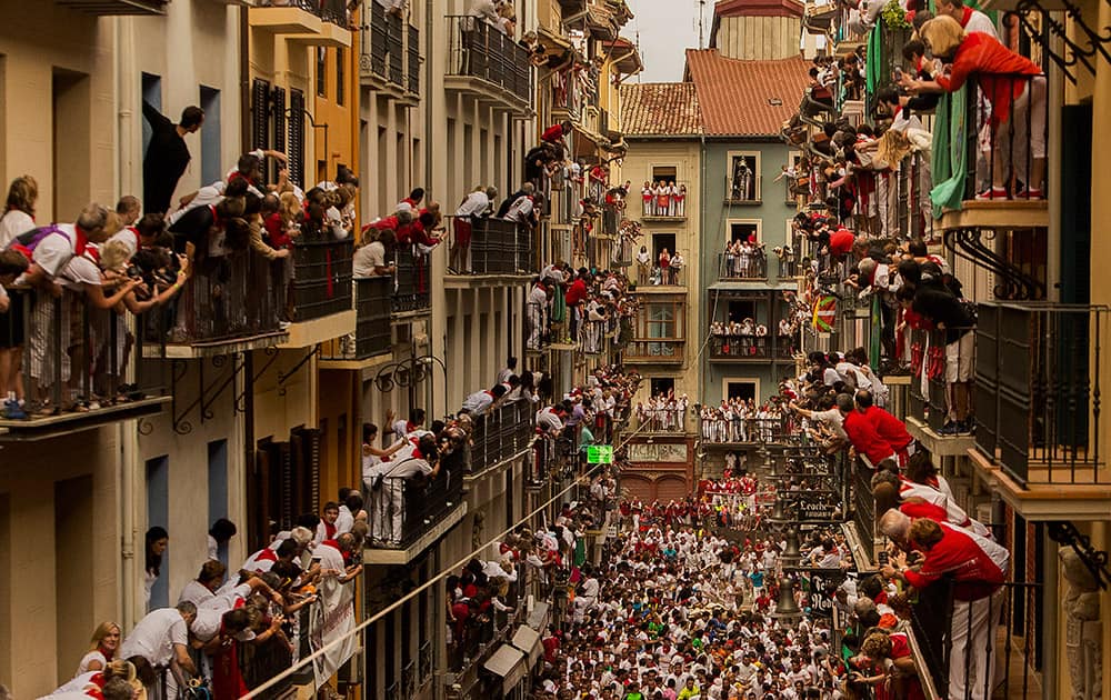 People watch as El Tajo y La Reina fighting bulls and revelers run during the running of the bulls, at the San Fermin festival, in Pamplona, Spain.