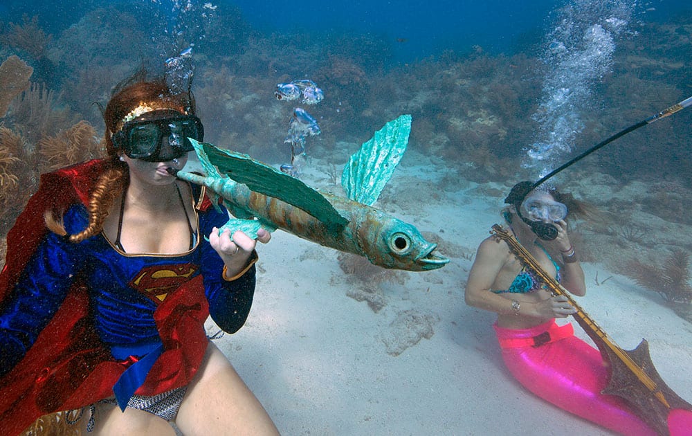 Kaitlin Goddard, left, costumed as superhero, blows through an artist's flying fish whistle, Saturday, July 11, 2015, during the Underwater Music Festival in the Florida Keys National Marine Sanctuary off Big Pine Key, Fla.