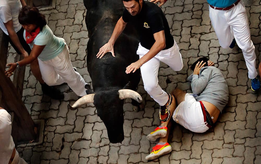 A fallen man covers his head while other revelers run alongside Garcigrande ranch fighting bulls during the daily morning running of the bulls of the San Fermin festival in Pamplona, Spain.