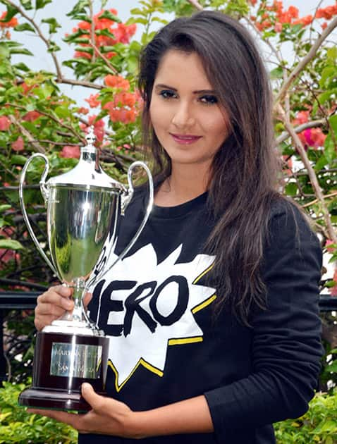 Sania Mirza poses for photographs with the Wimbledon doubles trophy that she won recently, at a news conference at her residence in Hyderabad.