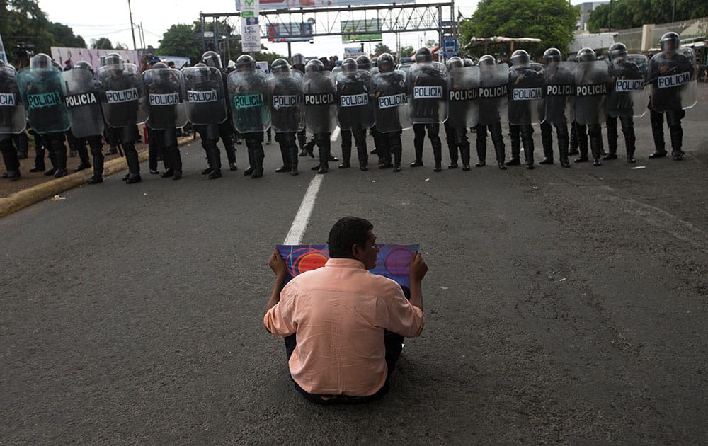 An anti-government protester sits before riot police, lined up near the Supreme Electoral Council, as he joins a demonstration demanding fair elections in Managua, Nicaragua.