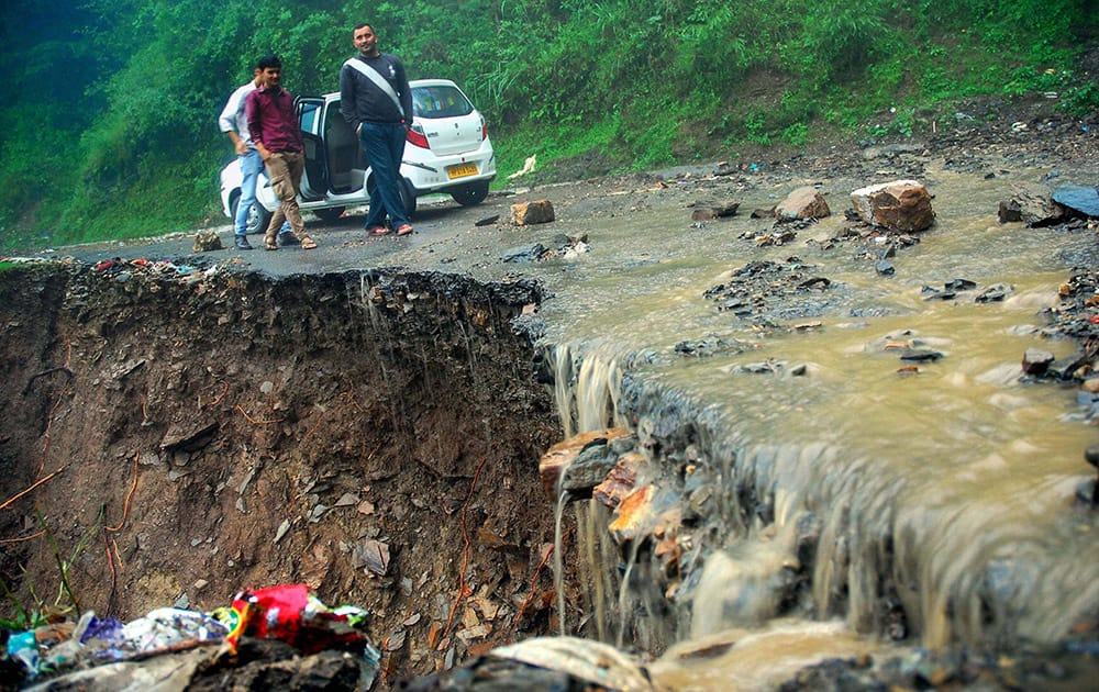 People stand near a washed off road after heavy rainfall at Banuti near Shimla.