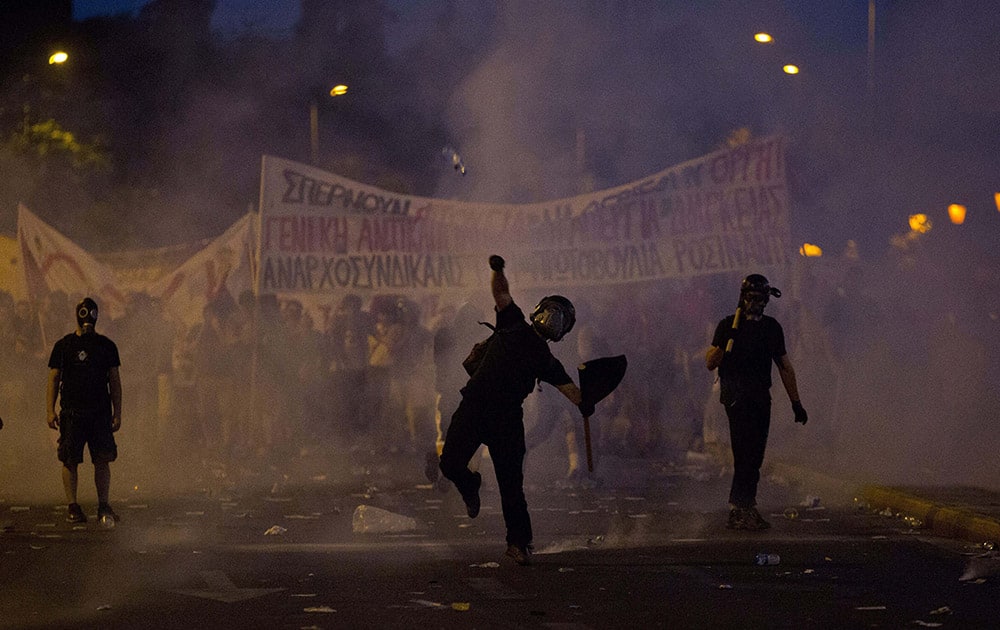 An anti-austerity protester throws a bottle at riot police in Athens. Greeces prime minister was fighting to keep his government intact in the face of outrage over an austerity bill that parliament must pass Wednesday night if the country is to start negotiations on a new bailout and avoid financial collapse. 