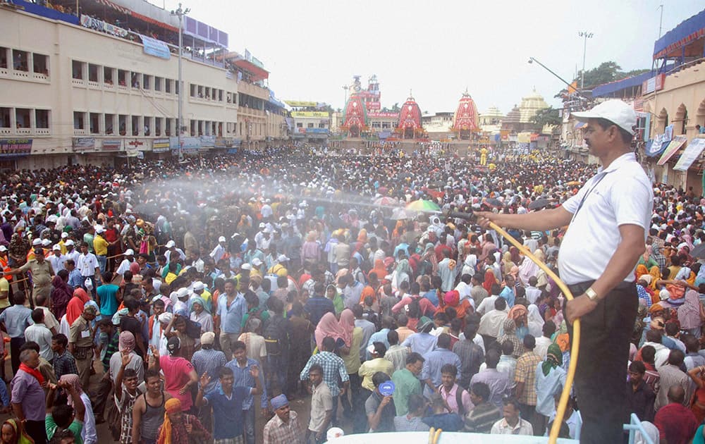 A volunteer sprays water on devotees during Nabakalebara Rathyatra in Puri.