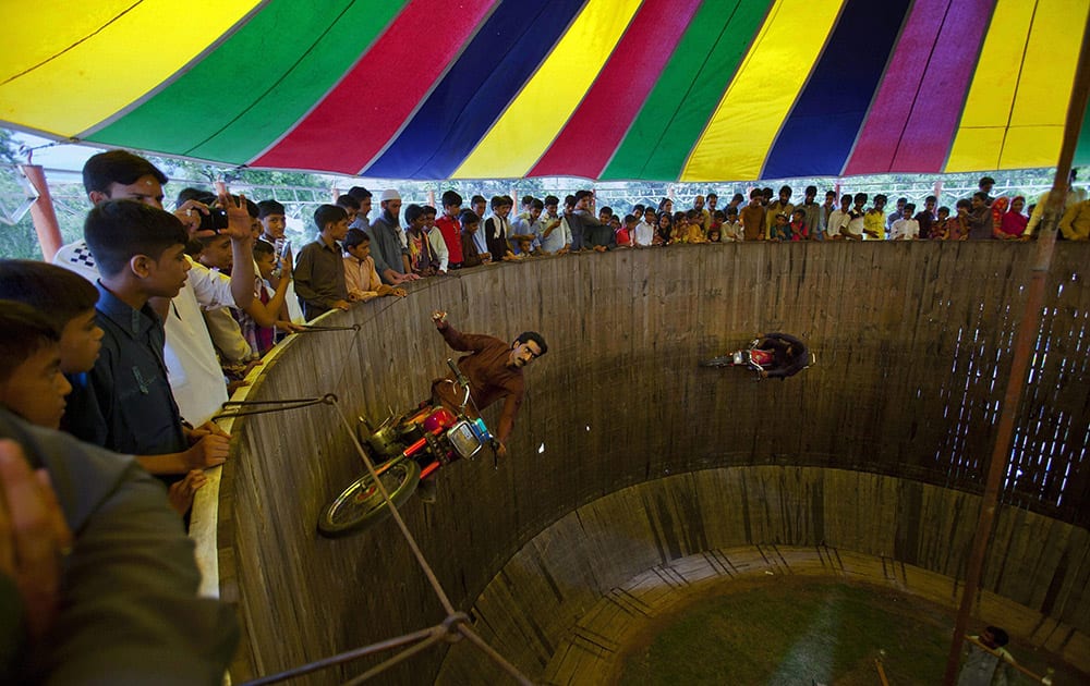 Pakistanis watch two performers demonstrate their motorcycle skills inside the well of death at a fair set up for the occasion of the Eid al-Fitr holiday in Rawalpindi, Pakistan.