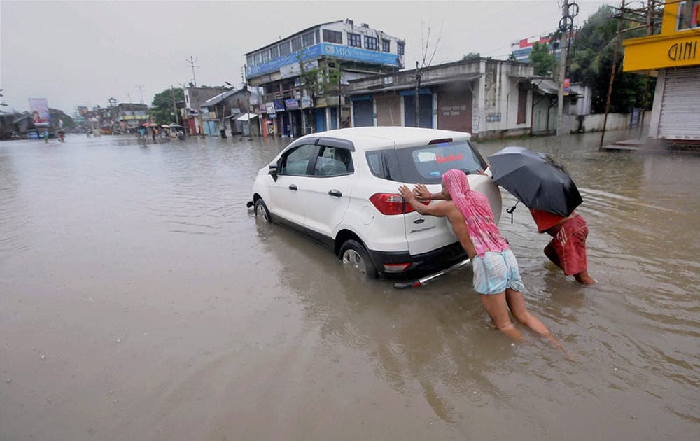 A car being pushed through a flooded street after rains in Agartala.