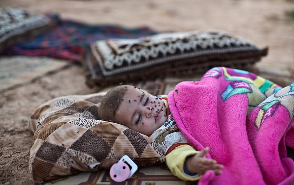 A Syrian refugee child, 4-month-old Marwa al-Hassan, her face covered with flies, sleeps on the ground outside her family's tent at an informal tented settlement near the Syrian border on the outskirts of Mafraq, Jordan.