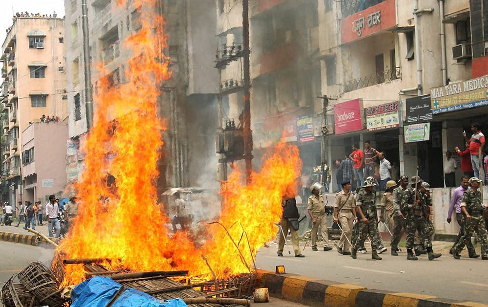 Security personnel patrol along a road as a road is blocked with fire during a bandh call demanding arrest of culprits responsibile for the eve-teasing, at Mango.