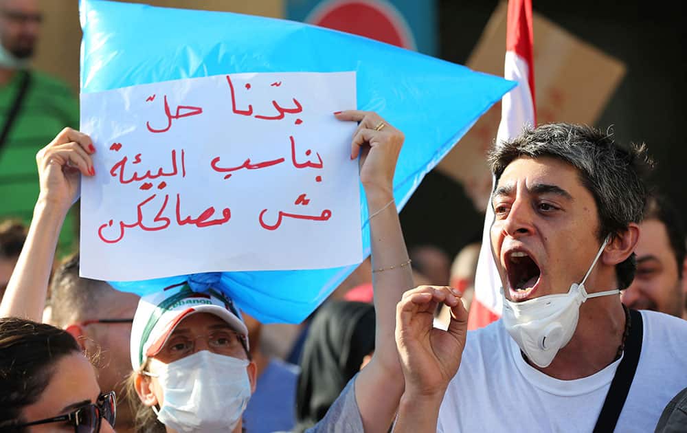 A Lebanese protester, right, shouts slogans as other in the left wears a trash bag with Arabic placard that reads: