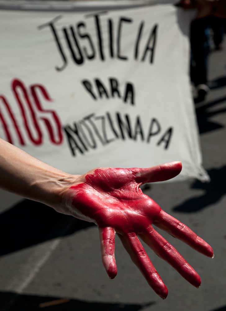 A woman shows a hand painted red in front of a banner that says: 