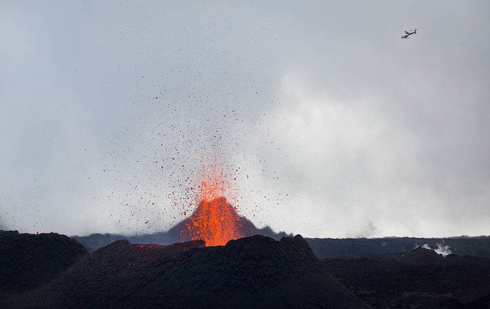 A helicopter flies over as lava erupts from the Piton de la Fournaise 