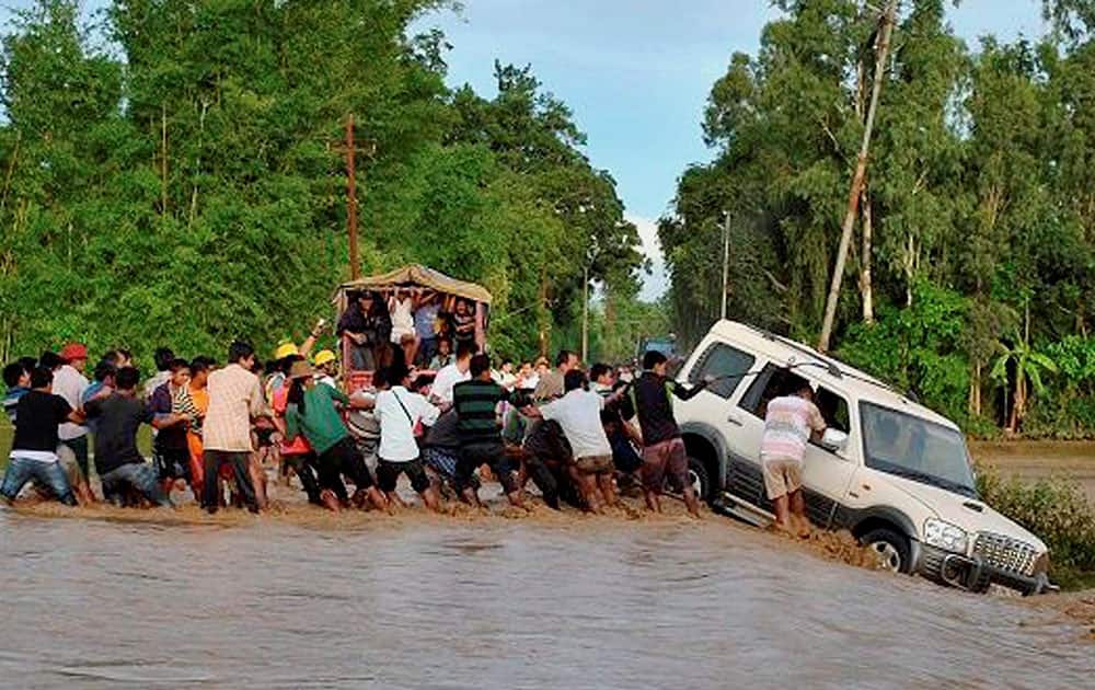 People try to retrieve a vehicle washed away by swirling flood waters following incessant rainfall in Thoubal district of Manipur.