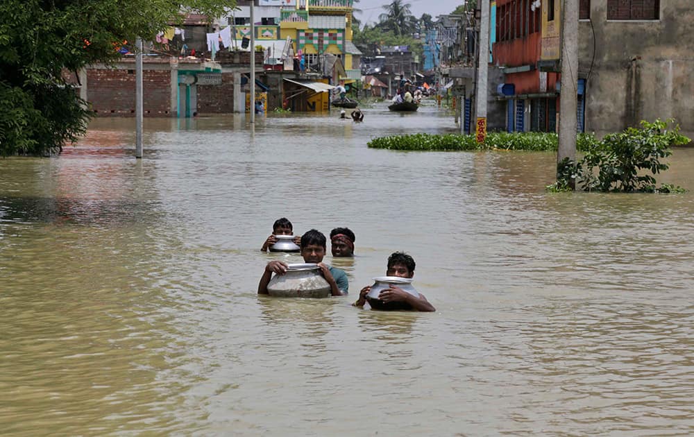 Villagers wade through flood waters with the help of empty utensils as they try to reach their house at Khanakul, about 100 kilometers (62 miles) west of Kolkata.