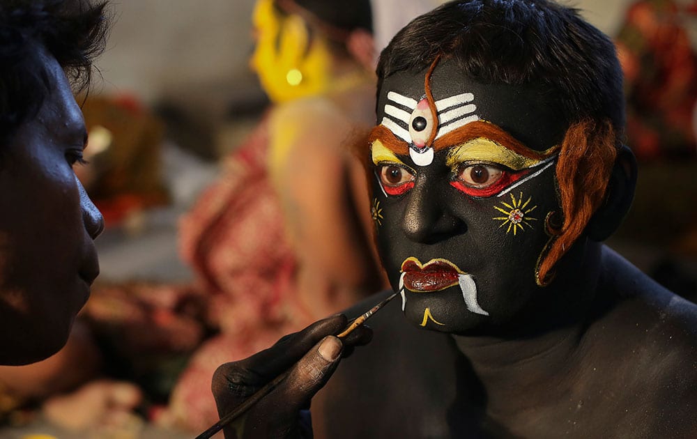 An Indian artist gets make up before a performance during a procession as part of 