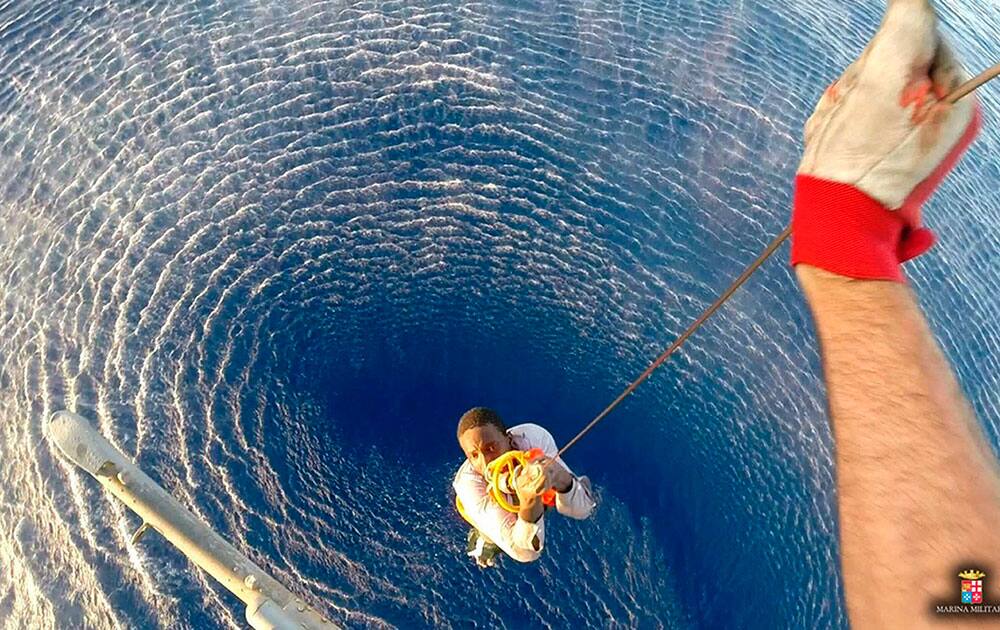 a migrant is lifted onboard by an helicopter from the Italian Navy ship Orione, after he and another migrant were spotted clinging to a barrel, in the Mediterranean sea, between Libya and Italy.