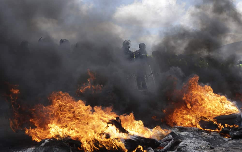 Security forces stand behind a burning road block set up by indigenous protesters from the highlands along the Panamerican Highway during a general strike in the Chasqui area of Ecuador.