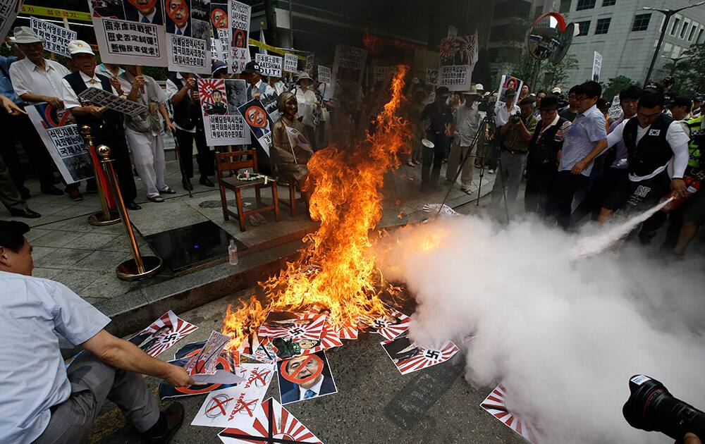 South Korean protesters burn defaced images of Japanese Prime Minister Shinzo Abe and Japanese rising sun flags as police officers spray fire extinguishers during a rally denouncing Abe's statement to mark the 70th anniversary of the end of World War II, near the Japanese Embassy in Seoul, South Korea.