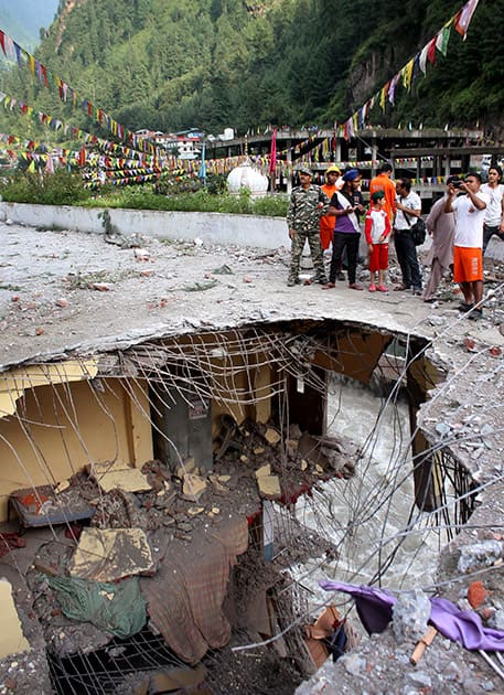 People take pictures of the damaged portion of a building near the historic Manikaran Sahib Gurudwara, seen in the background, after it was affected by a landslide near Kullu, Himachal Pradesh.