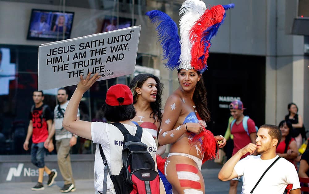 a proselytizer walks by two women clad in thongs and body paint in Times Square, in New York. New York City Mayor Bill de Blasio is promising to take action against women who pose nearly naked for photos in Times Square in exchange for cash.