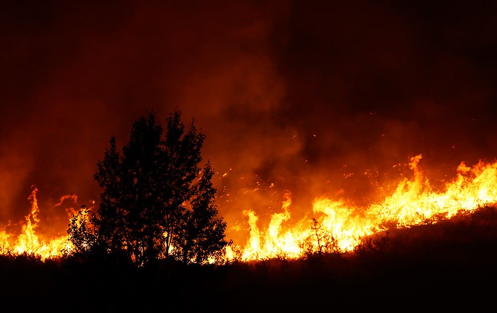 Flames rise near a tree on the ridge line above several homes on Twisp River Road just after midnight, in Twisp, Wash. 