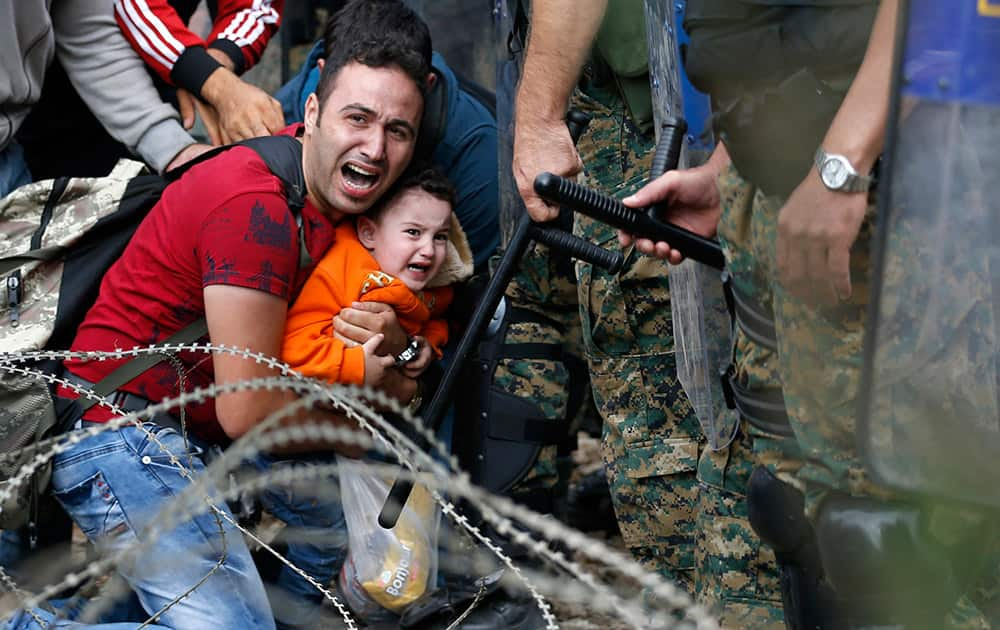 A migrant man holding a boy react as they are stuck between Macedonian riot police officers and migrants during a clash near the border train station of Idomeni, northern Greece, as they wait to be allowed by the Macedonian police to cross the border from Greece to Macedonia.