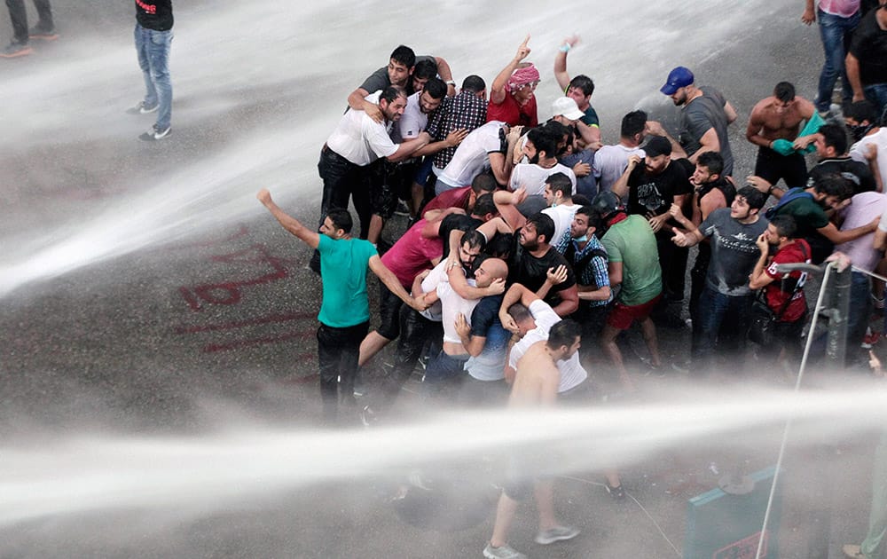 Lebanese activists shout anti-government slogans as they are sprayed by riot police using water cannons during a protest against the ongoing trash crisis, in downtown Beirut, Lebanon.