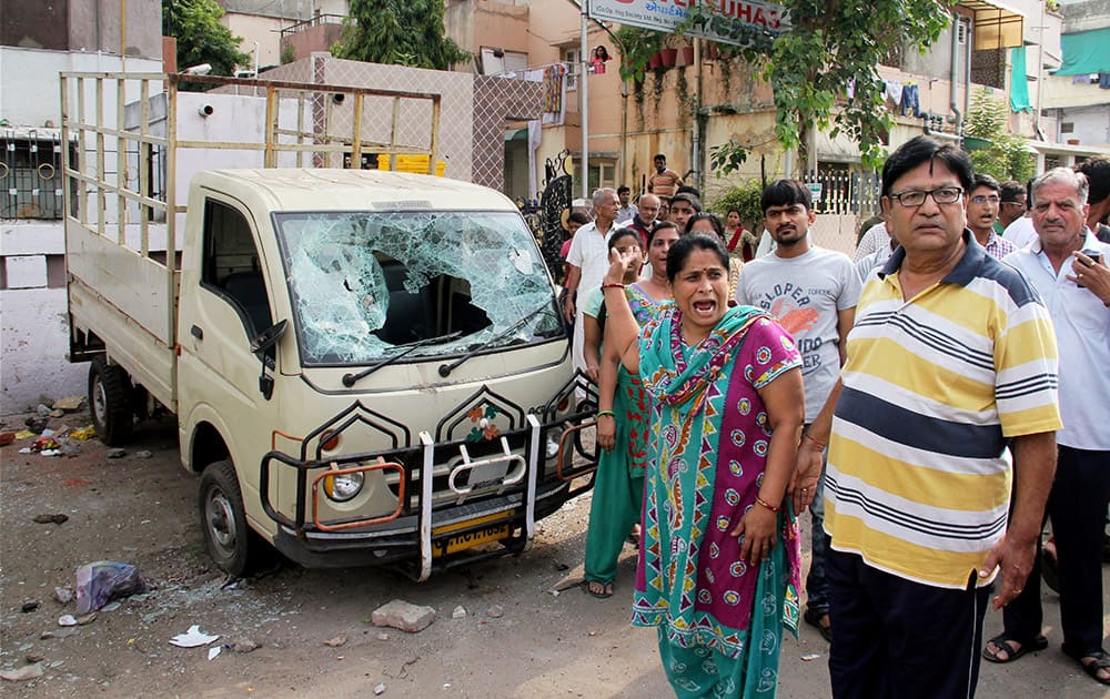 People stand in front of a damaged vehicle after violent clashes between Patel community and OBC members at Juna Wadaj locality in Ahmedabad.