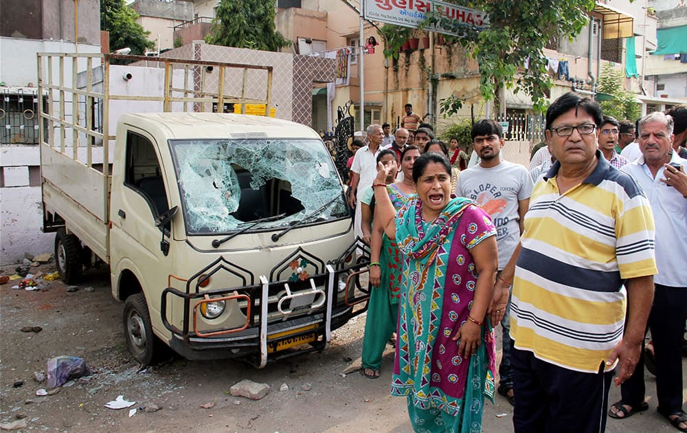 People stand in front of a damaged vehicle after violent clashes between Patel community and OBC members at Juna Wadaj locality in Ahmedabad.