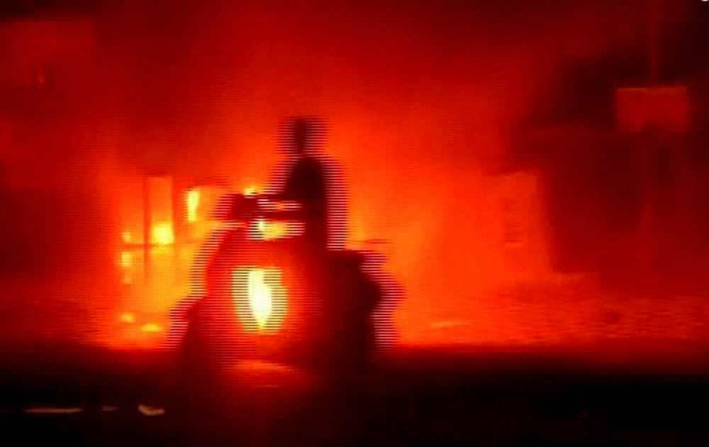 TV Grab- A biker moves past a burning vehicle set on fire in Ahmedabad on Tuesday by people after the arrest of Hardik Patel, convener of Patidar Anamat Andolan Samiti.