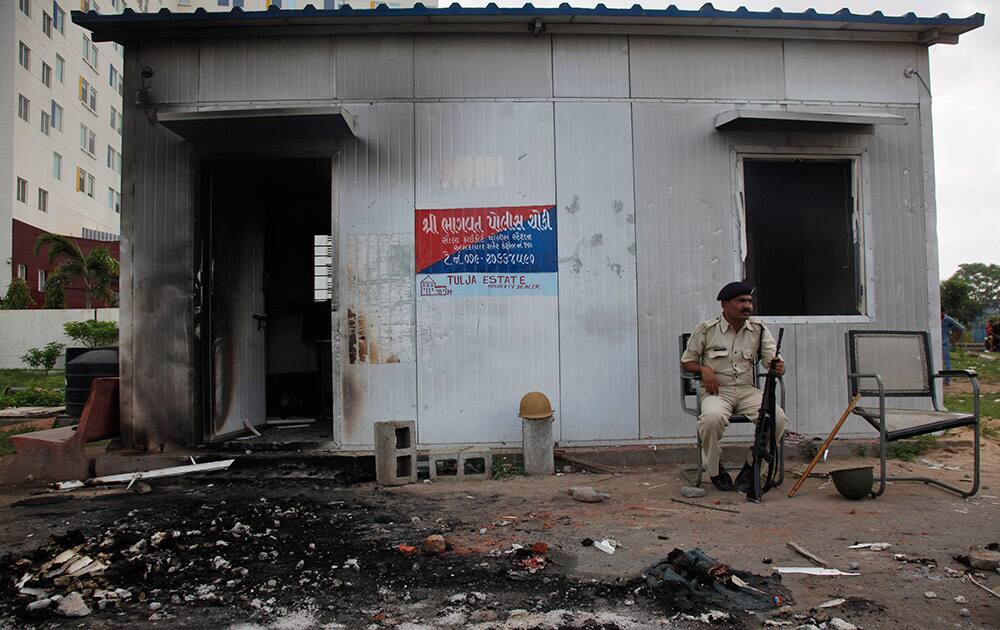 A policeman sits outside a damaged police post that was set on fire during clashes in Ahmedabad.