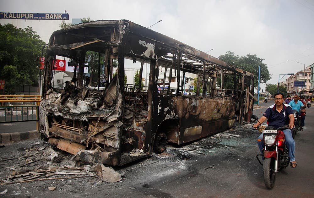 Commuters pass by a damaged bus which was set on fire during clashes in Ahmedabad.