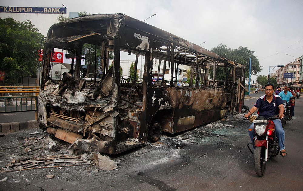 Indian commuters pass by a damaged bus which was set on fire during clashes in Ahmadabad, India