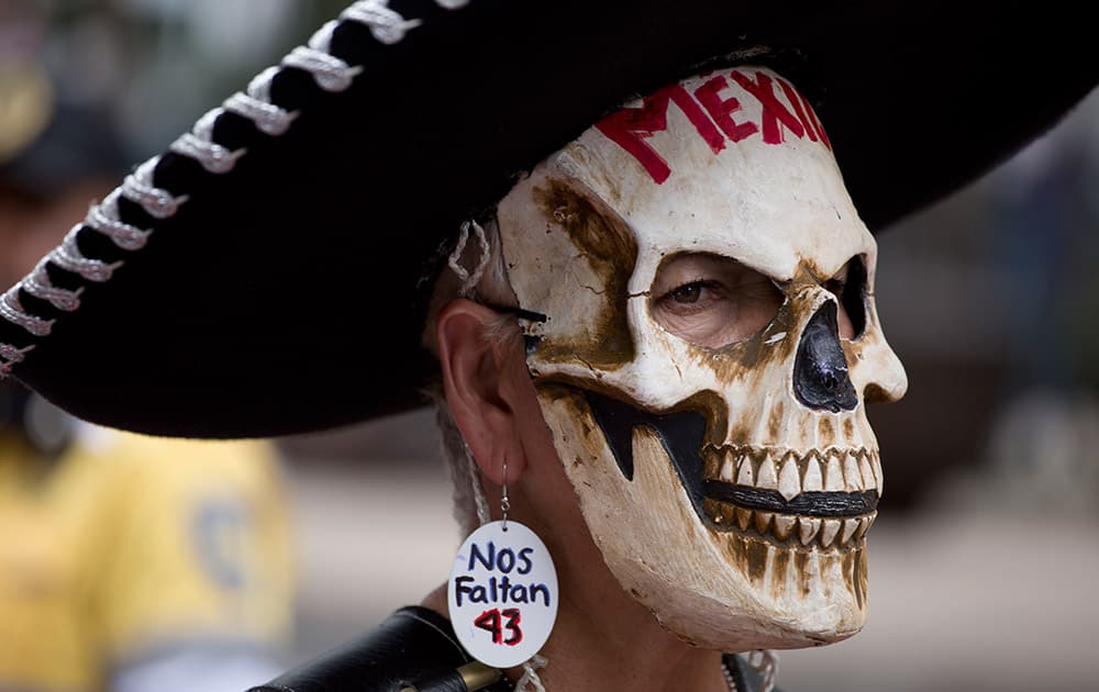 A demonstrator wears a Mexican Charro hat, a skull mask and an earring with text that reads in Spanish 