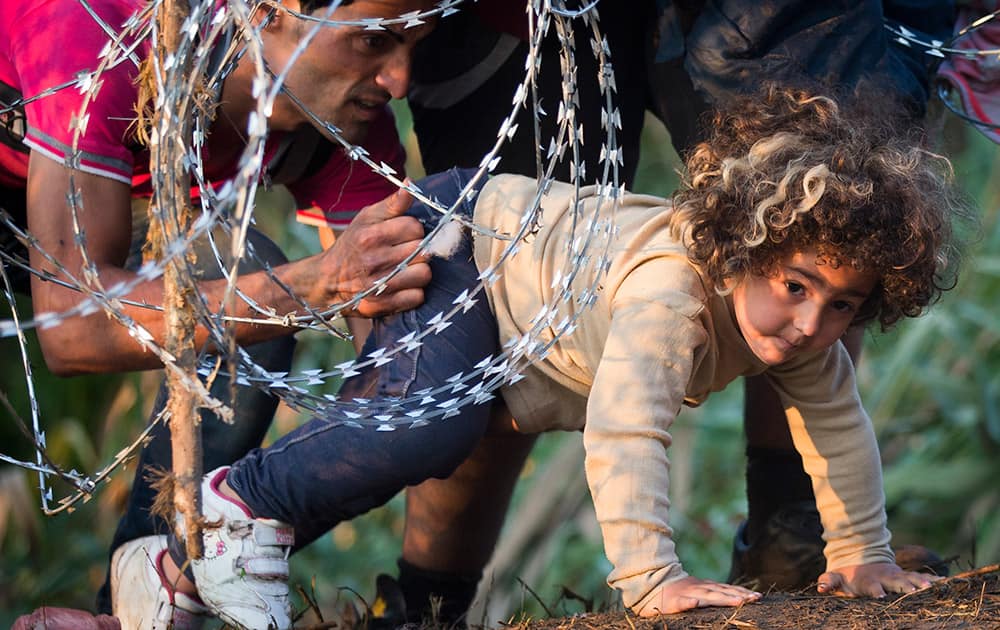 A refugee girl moves under barbed wire as she crosses from Serbia to Hungary, in Roszke.