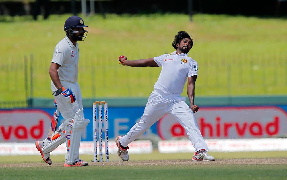 Sri Lanka's Nuwan Pradeep bowls a ball as India's Rohit Sharma, left, watches on day four of the third cricket test match in Colombo, Sri Lanka.