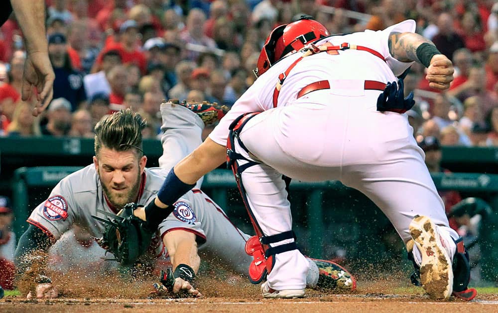 Washington Nationals' Bryce Harper, left, scores ahead of the tag from St. Louis Cardinals catcher Yadier Molina during the first inning of a baseball game.