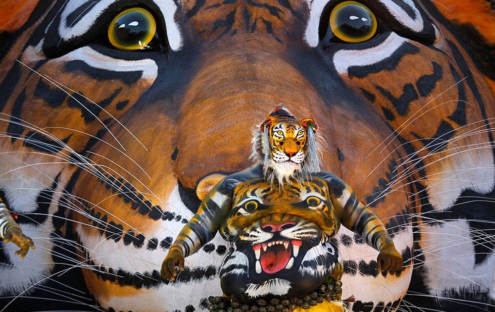 An Indian artist with his body painted with the likeness of a tiger dances before a tableau with a picture of tiger during the 'Pulikali' or Tiger Dance procession in Thrissur, Kerala state, India.