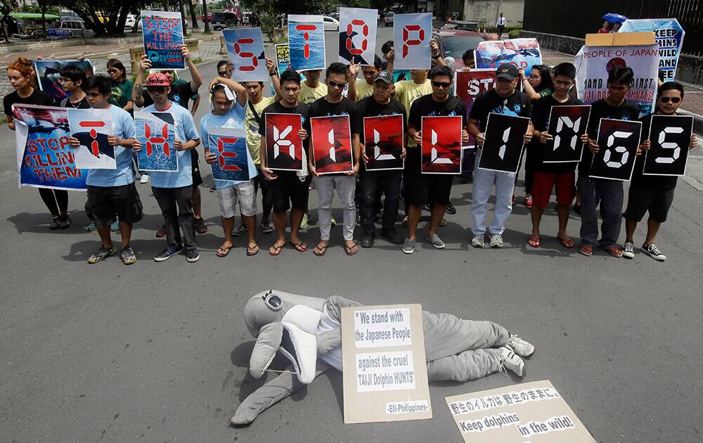 An activist in dolphin mascot lies on the ground as environmental activists form the slogan 