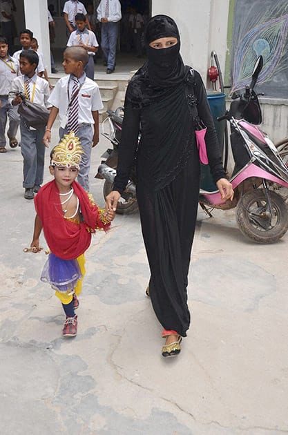 A muslim woman walks with her child dressed up as Lord Krishna to take part in a program at school ahead of Janmashtami festival in Mirzapur.