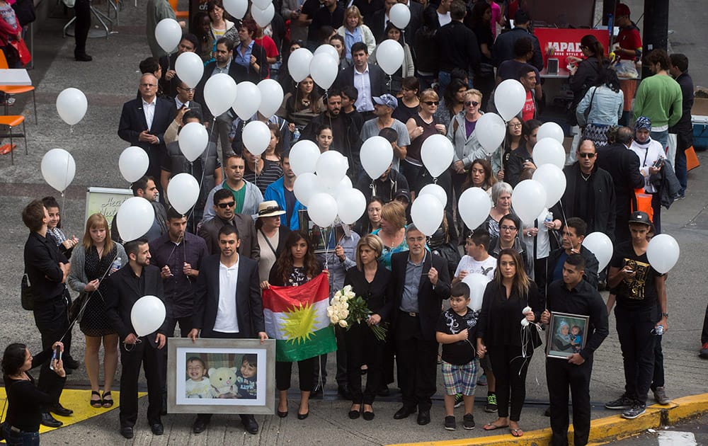 Tima Kurdi, foreground center, aunt of late brothers Alan and Ghalib Kurdi, her husband Rocco Logozzo, center right, son Alan Kerim, bottom left, holding photo, and family friend, Nissy Koye, holding flag, walk to the waterfront to release balloons in memory of the boys after a memorial service in Vancouver, British Columbia, Canada.