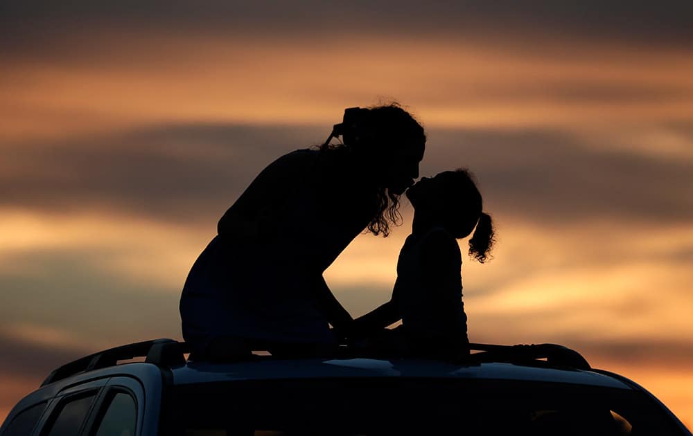 Savannah Anderson, left, kisses her sister Macy Saunders, 6, as they sit on top of a car to view a sunflower field at sunset near Lawrence, Kan. 