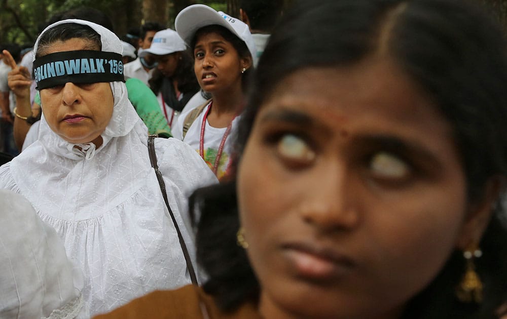 A participant, center looks as a blindfolded woman, left joins a partially blind girl, right, during the Bangalore Blindwalk in Bangalore.