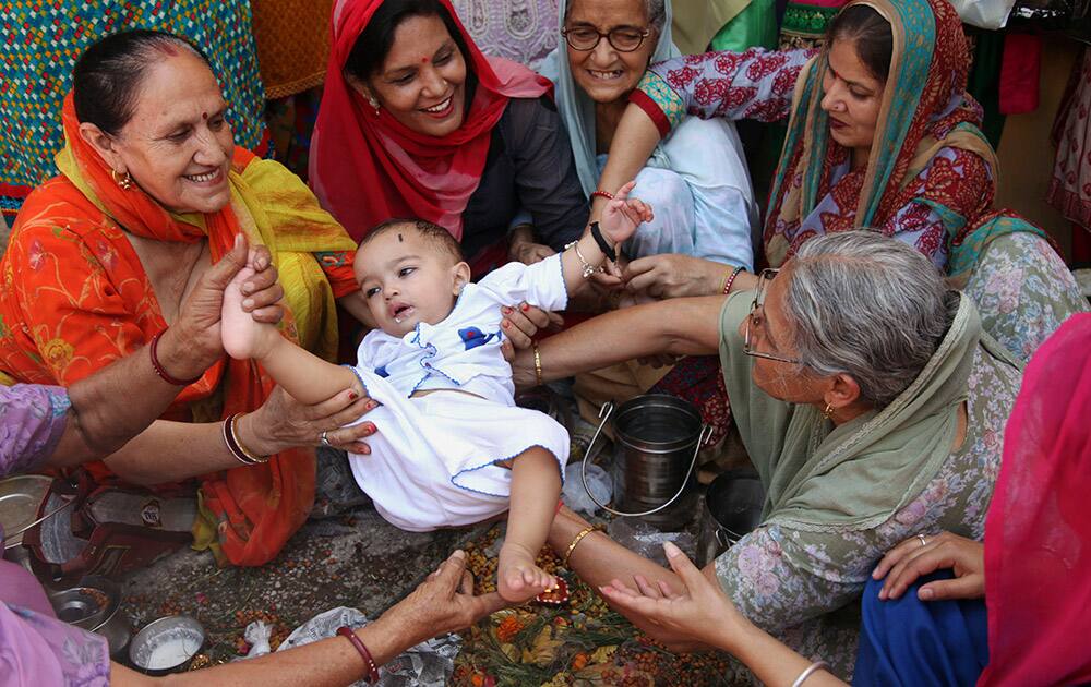 Hindu women belonging to the Dogra community swing a child as part of a ritual as they pray for the long life of their sons during the 