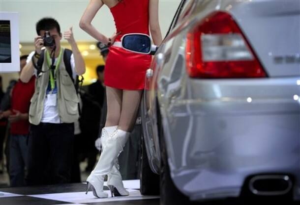 A visitor gestures while taking souvenir photos of a model posing at the Beijing auto show