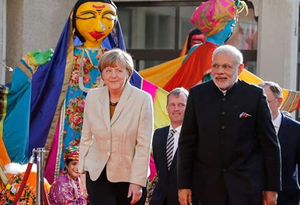 German Chancellor Angela Merkel, left, welcomes India's Prime Minister Narendra Modi, right, as a traditional Indian music group performs at the opening of the industrial fair in Hanover, Germany, Sunday, April 12, 2015.